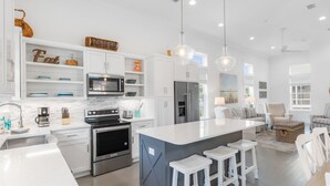 Une cuisine moderne avec des meubles blancs, des appareils en acier inoxydable et un îlot central doté de tabourets de bar.