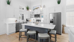 A modern kitchen with white cabinetry, a central island with bar stools, stainless steel appliances, and hanging pendant lights.
