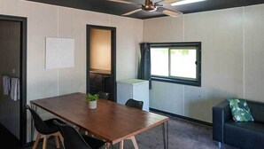 Una habitación con una mesa de madera, sillas negras, un ventilador de techo, una ventana y un sofá.