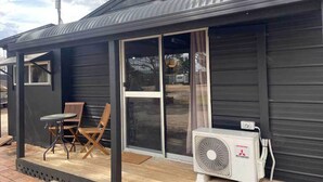 Un edificio pequeño con puerta de vidrio corredera, un ventilador y un patio con sillas.