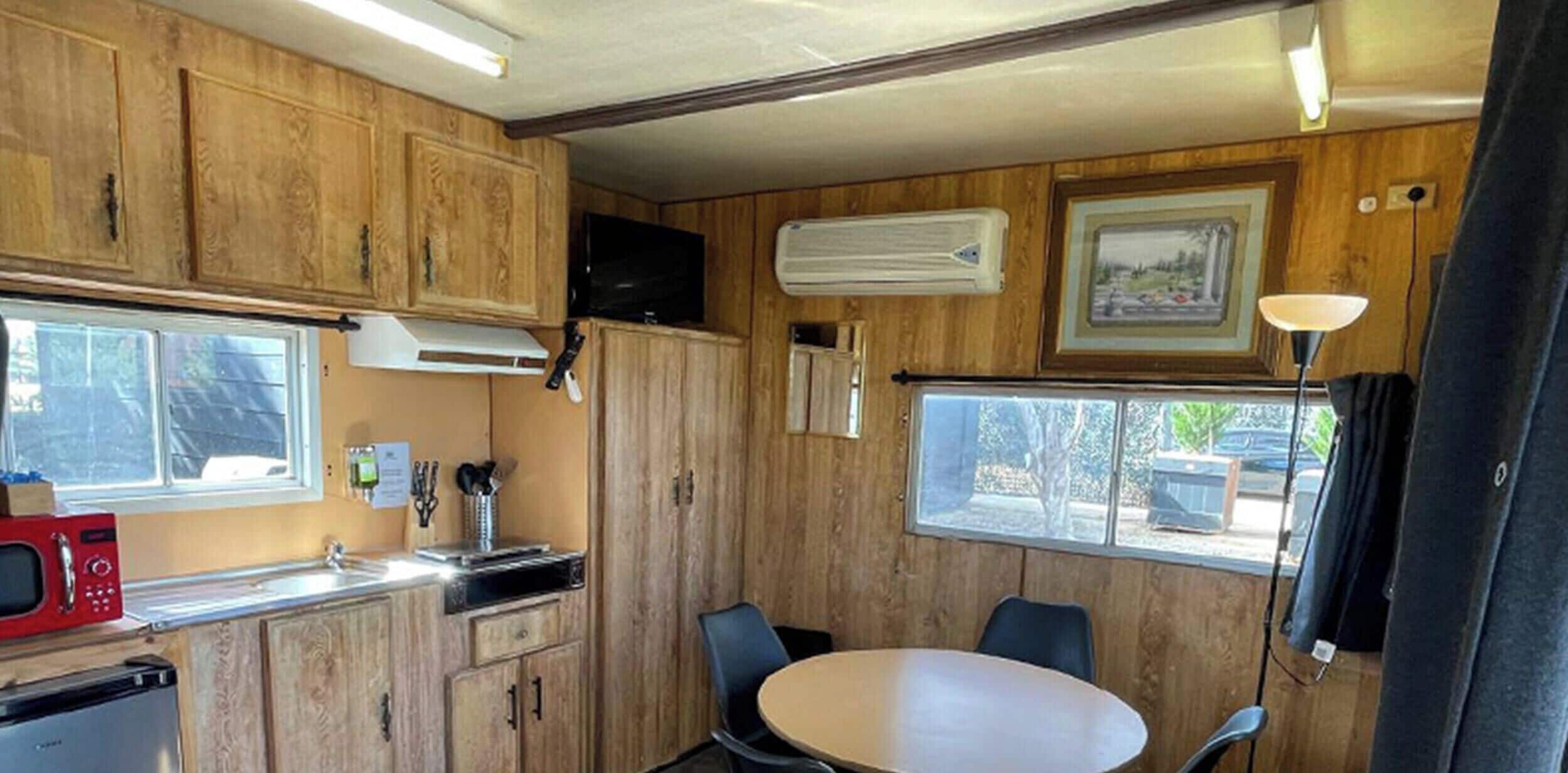 Una cocina compacta con armarios de madera, un microondas, un lavamanos y una zona de comedor con una mesa y sillas.