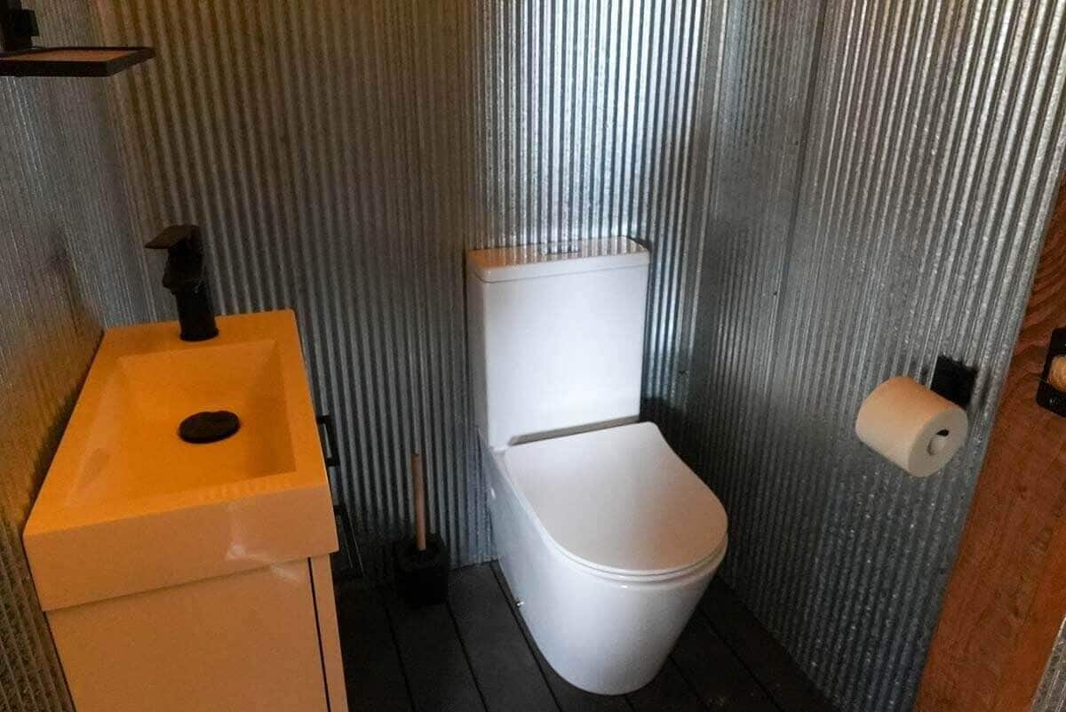 A small bathroom with a white toilet, a yellow sink, and a roll of toilet paper on the wall.
