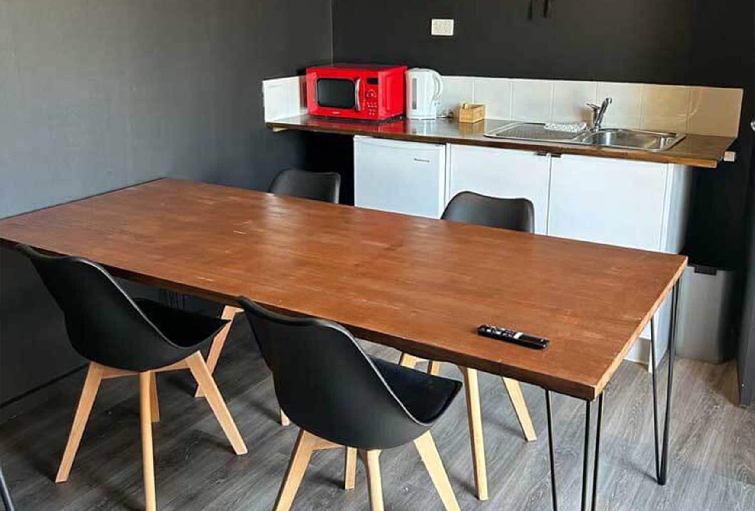 A compact kitchen with a microwave, coffee maker, and sink. There is a wooden dining table with two chairs.