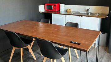 A compact kitchen with a microwave, coffee maker, and sink. There is a wooden dining table with two chairs.