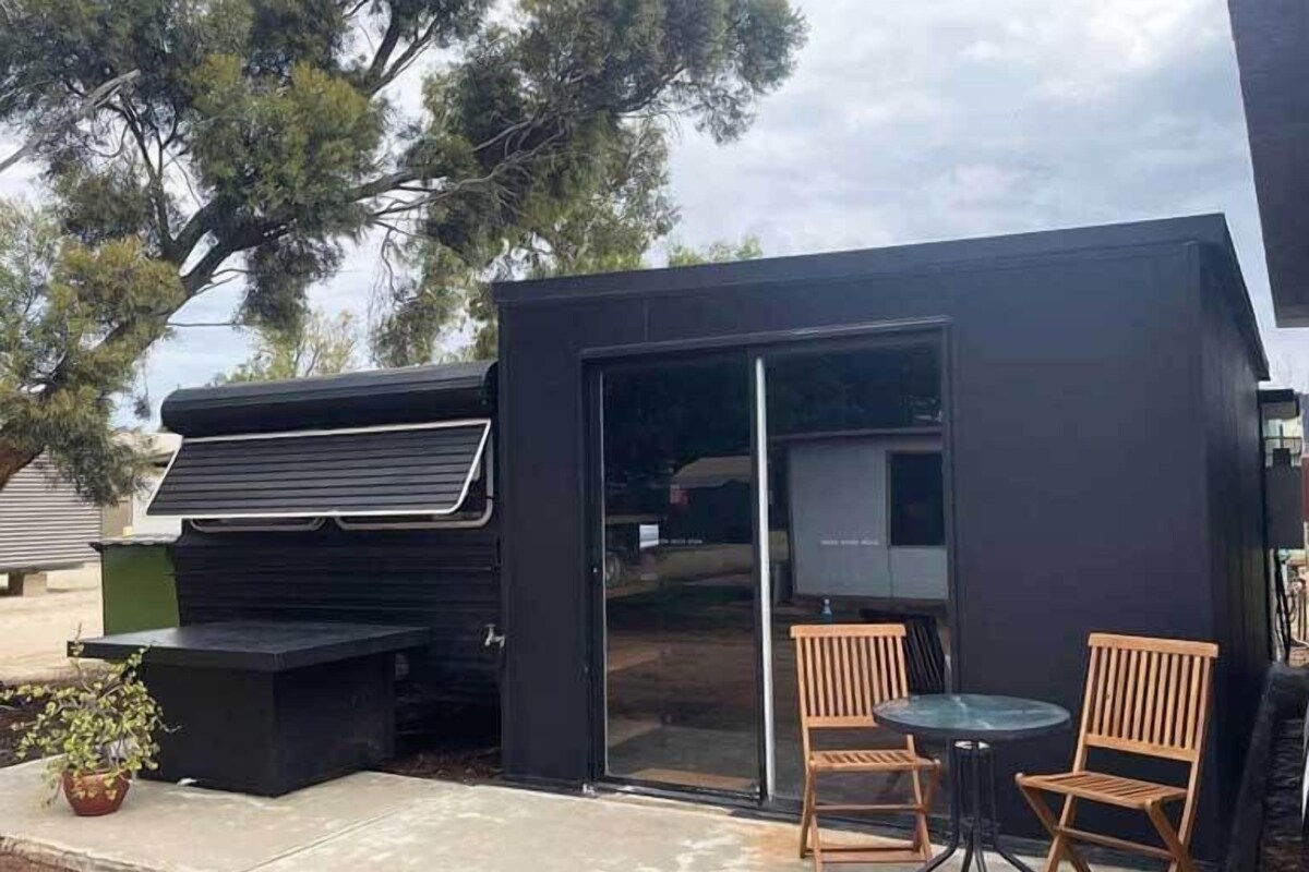 A modern outdoor patio with a grill, two wooden chairs, and a glass door leading to a covered area.