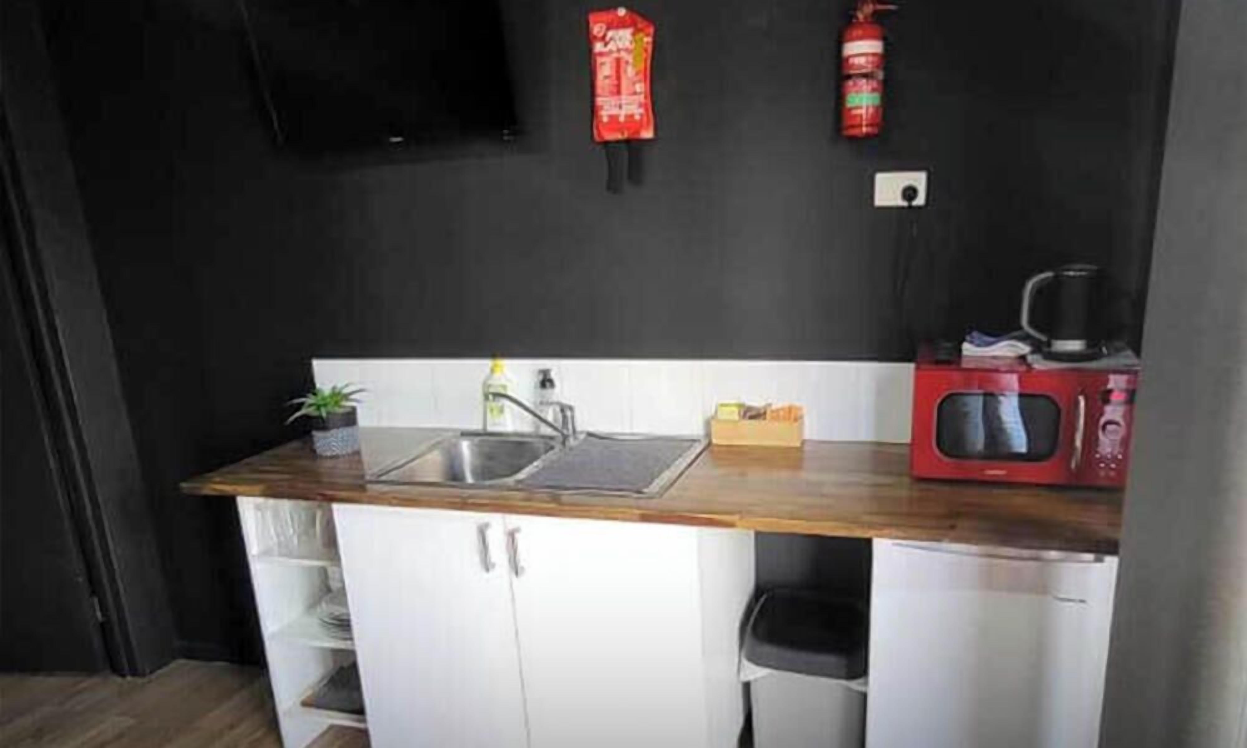 Una cucina compatta con piano di lavoro in legno, lavello, forno a microonde ed estintore.