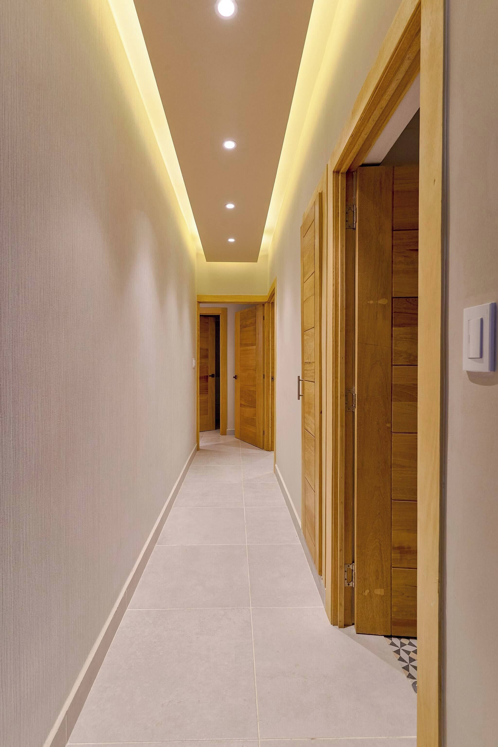 Un pasillo con piso de baldosas, puertas de madera e iluminación empotrada en el techo.
