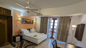 A bedroom with a bed, a desk, a chair, a ceiling fan, and a window with curtains. - Lux Suites Lamera Beachfront Apartments (Mombasa)