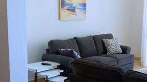 A living room with a dark-colored sofa, a small white table, and a painting on the wall. - Lux Suites Lamera Beachfront Apartments (Mombasa)