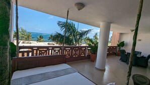 A balcony with a bed, potted plants, and a view of the ocean. - Lux Suites Lamera Beachfront Apartments (Mombasa)
