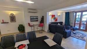 A modern living room with a black dining table, red chairs, a blue sofa, and a large window with curtains. - Lux Suites Lamera Beachfront Apartments (Mombasa)