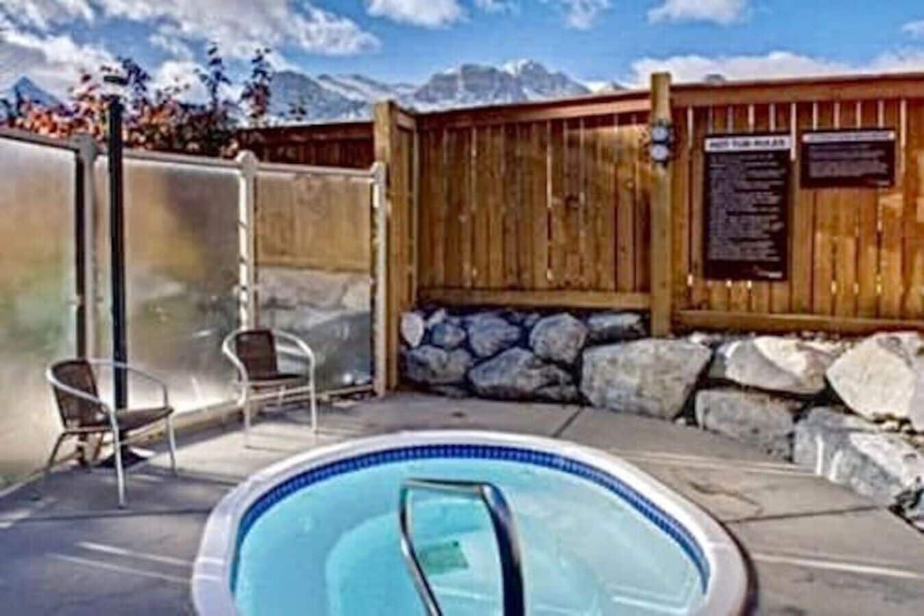 A pool area with a wooden fence, stone wall, and two chairs.