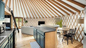 A modern yurt interior with a kitchen, dining area, and a cozy seating space. - Scenic forest yurt w/ hot tub & river access (Wardensville)
