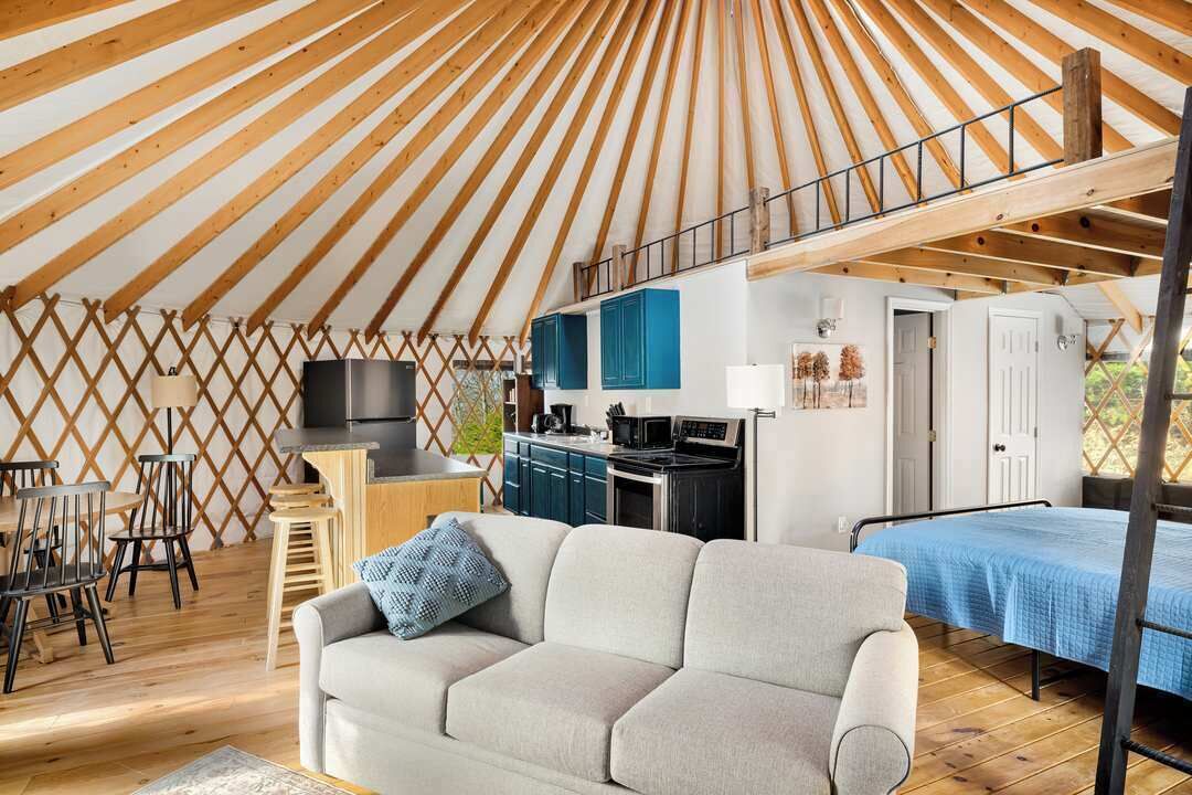 Una yurta espaciosa con techo alto, zona de cocina, sofá y cama.