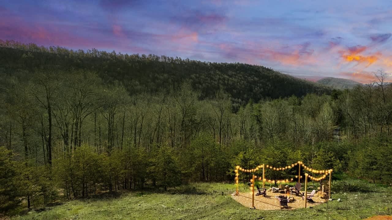 Ein bewaldetes Gebiet mit einer kleinen Lichtung, auf der sich ein Gazebo mit Lichterketten und Gartenmöbeln befindet.