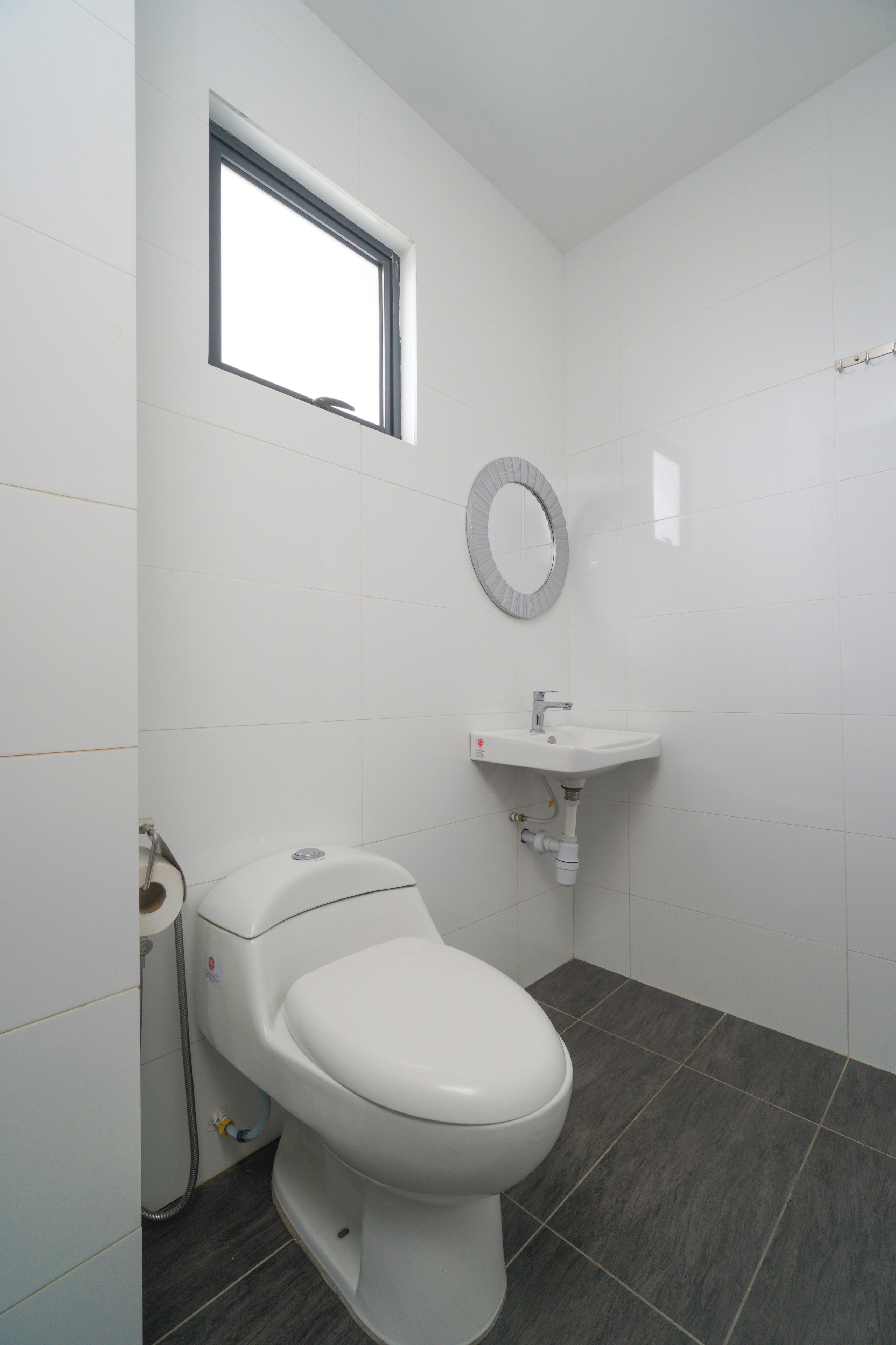A bathroom with a toilet, a sink, a mirror, and a window.