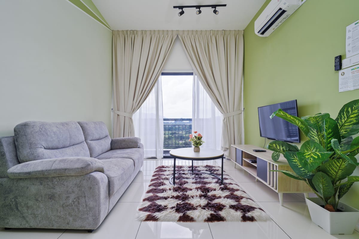 A modern living room with a grey sofa, a white coffee table, a large potted plant, and a television on the wall.