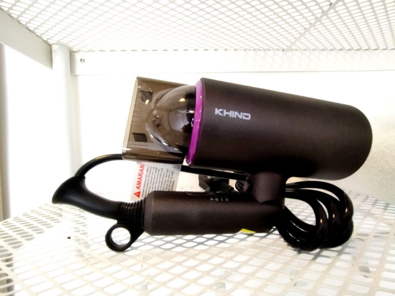 A black hairdryer with a purple accent on a white, grid-patterned surface.