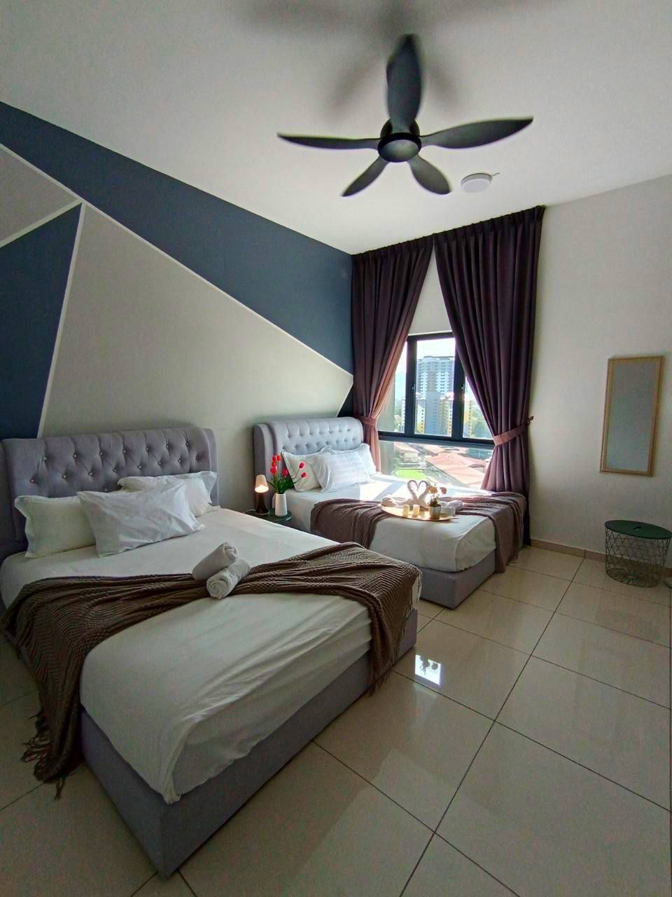 Habitación de hotel con cama, ventilador de techo, ventana con cortinas y vistas a edificios.