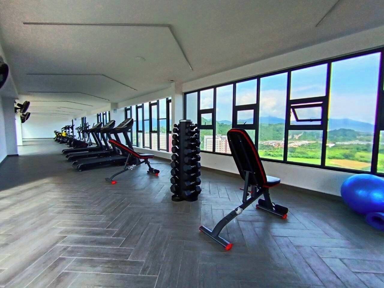 Een sportschool met trainingsapparatuur, grote ramen en uitzicht op de omgeving.