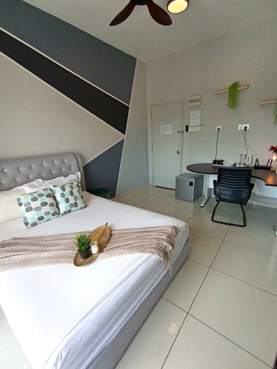 Habitación de hotel moderna con cama, una mesita, una silla, un ventilador de techo y una puerta.