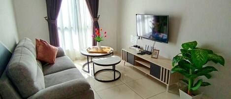 A living room with a sofa, a chair, a TV, a ceiling fan, and an air conditioning unit.