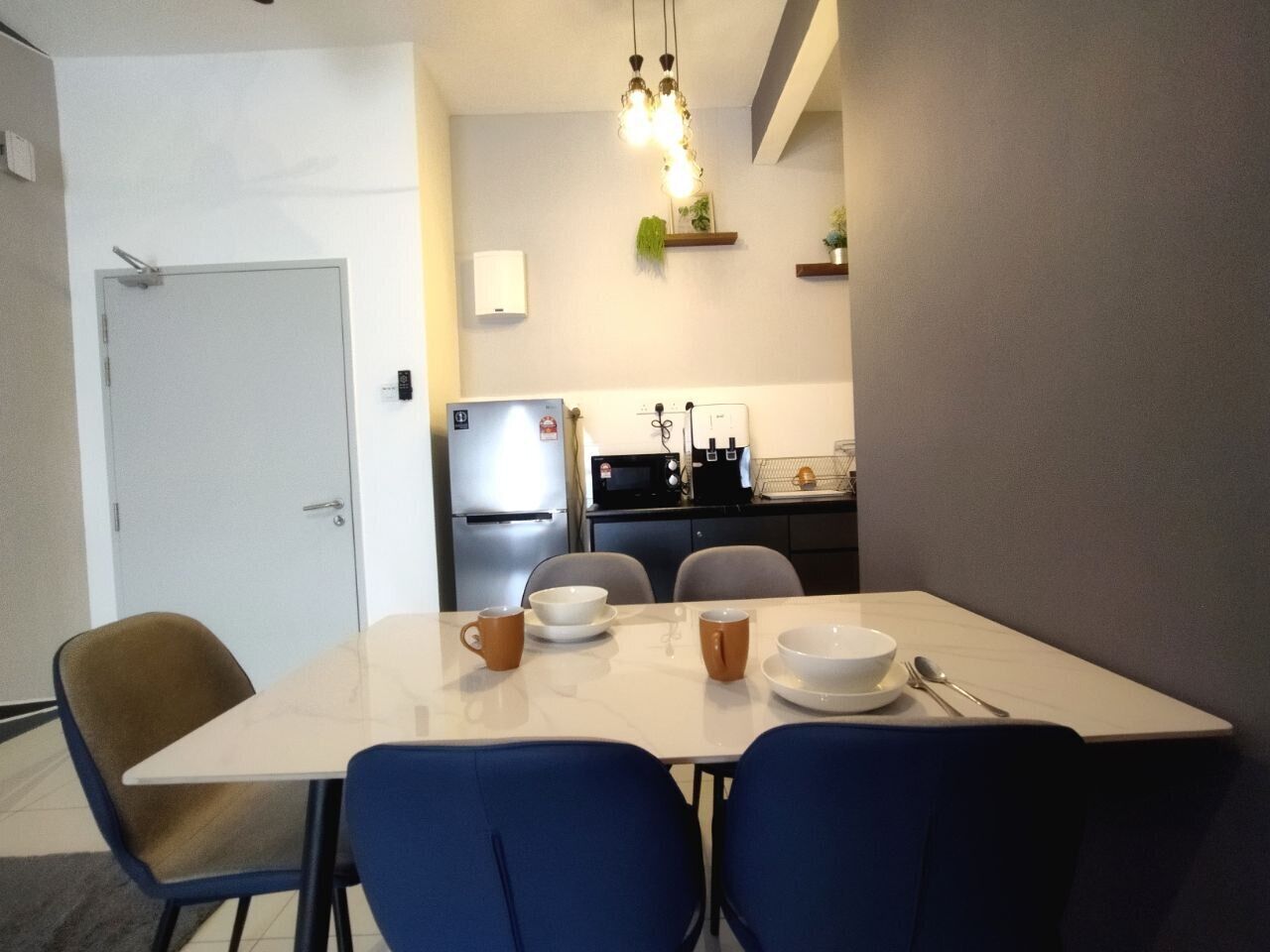 Un coin repas avec une table dressée pour quatre personnes, des chaises, un réfrigérateur, un four à micro-ondes et un petit comptoir de cuisine avec un évier.