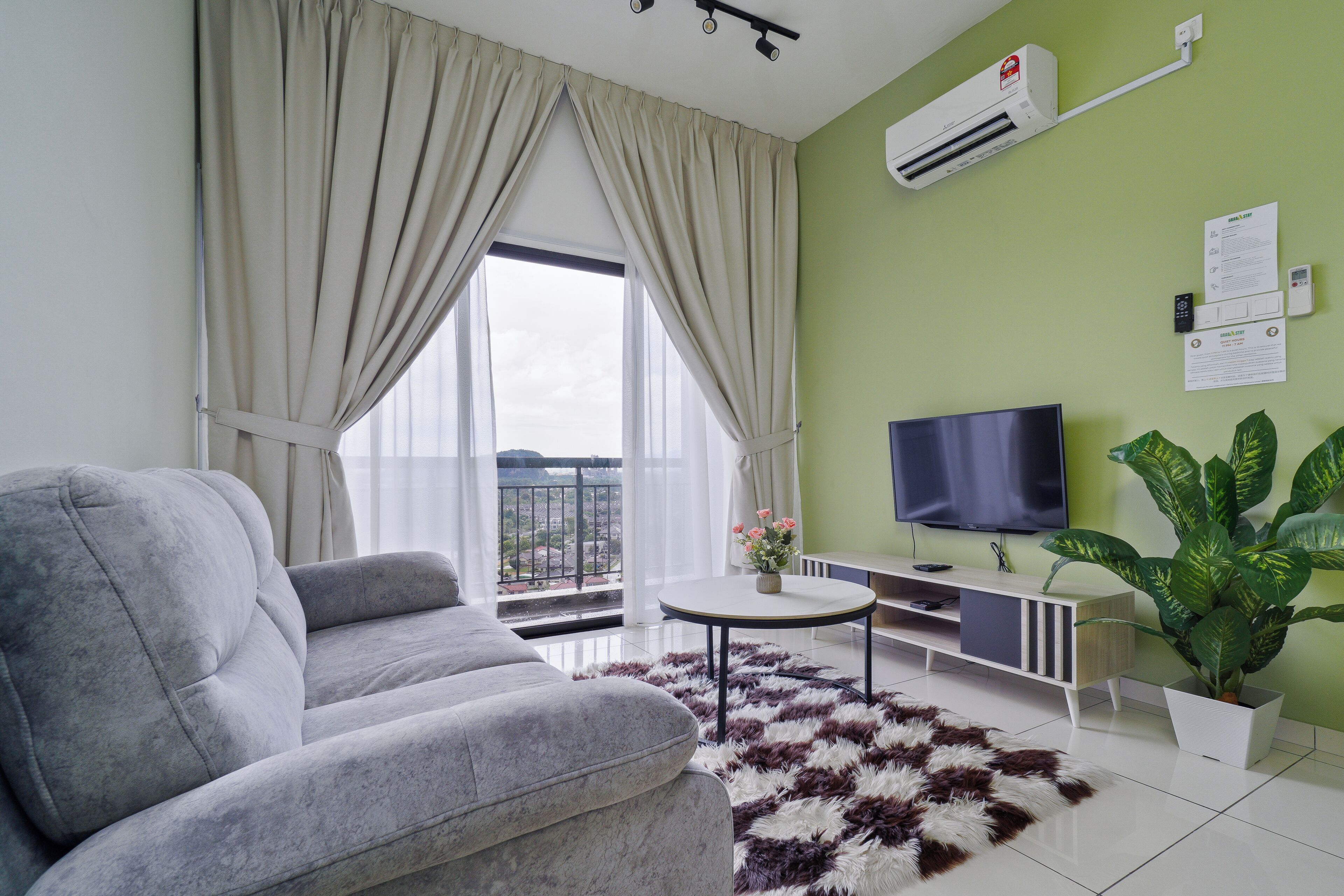 A modern living room with a grey sofa, a round coffee table, a TV, and a large potted plant.