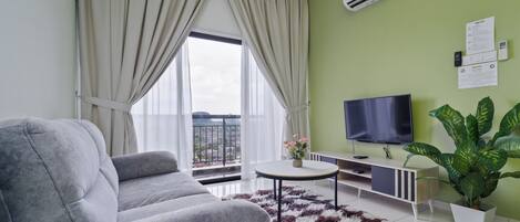 A modern living room with a grey sofa, a round coffee table, a TV, and a large potted plant.