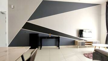 Una sala de estar moderna con un diseño geométrico en la pared, un televisor de pantalla plana, una mesa de centro negra y un sofá gris.