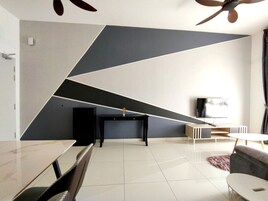 Una sala de estar moderna con un diseño geométrico en la pared, un televisor de pantalla plana, una mesa de centro negra y un sofá gris.