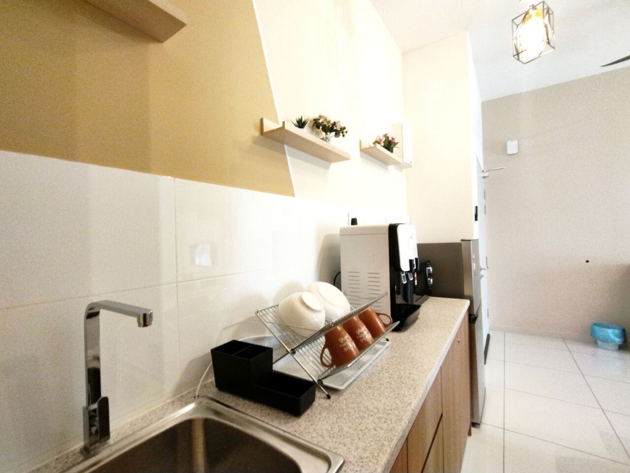 A modern kitchen with a stainless steel sink, a coffee machine, and a small shelf with decorative items.