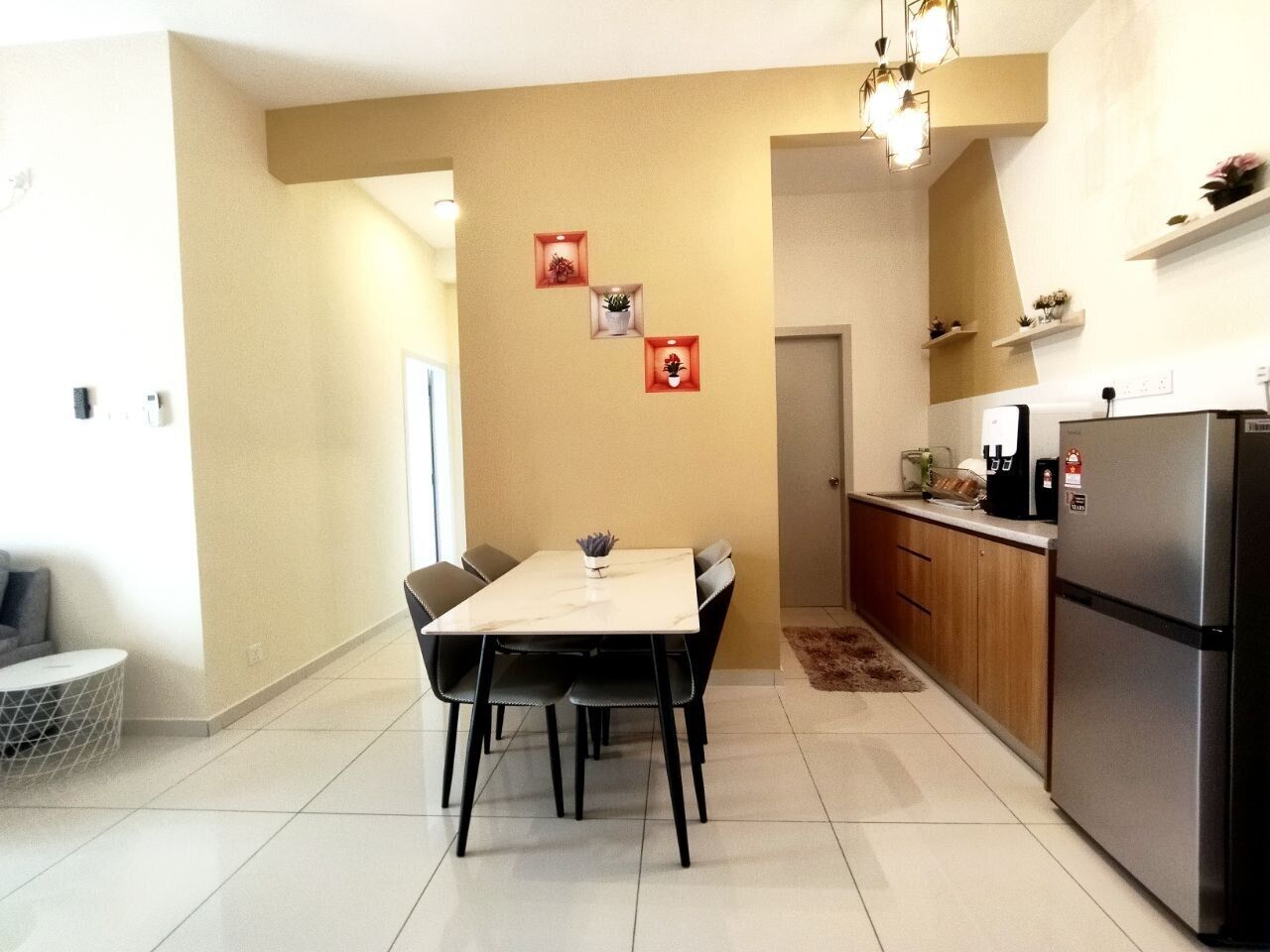 A modern kitchen with a dining area, featuring a marble table, black chairs, a refrigerator, and a coffee machine.