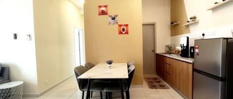 A modern kitchen with a dining area, featuring a marble table, black chairs, a refrigerator, and a coffee machine.