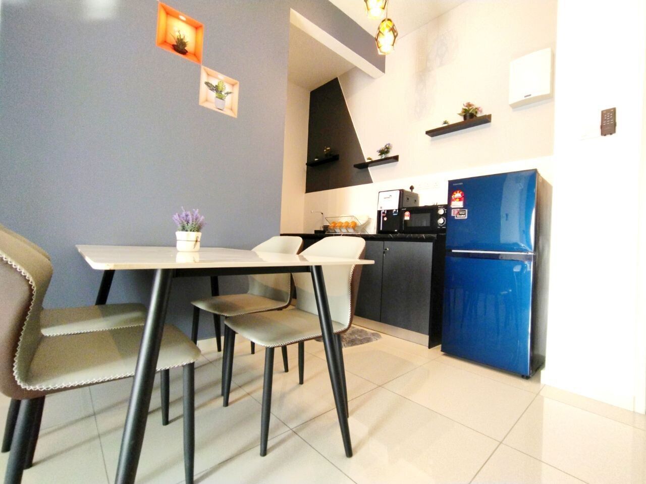 A dining area with a table and chairs, a kitchen with a blue refrigerator, and a wall-mounted shelf with small plants.
