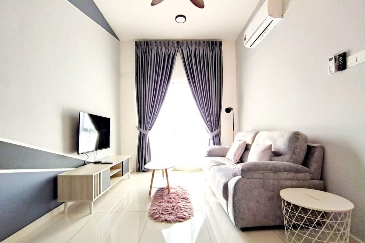 A modern living room with a flat-screen TV, grey sofa, and a round side table.