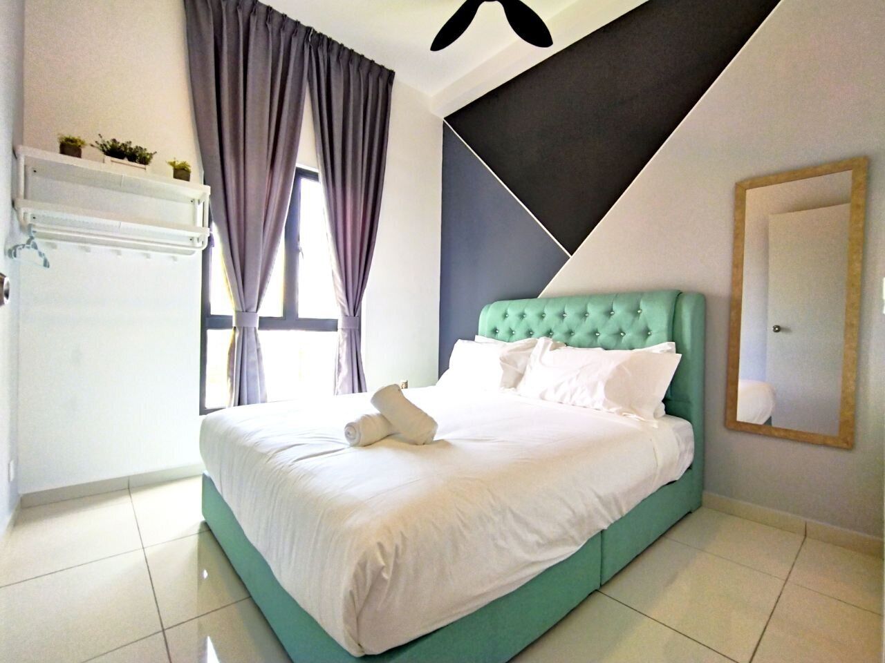 A neatly made bed with white linens and pillows, a teal headboard, and a window with curtains.