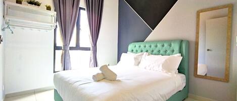 A neatly made bed with white linens and pillows, a teal headboard, and a window with curtains.