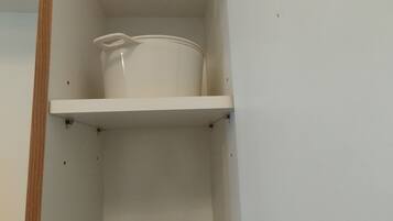 A kitchen cabinet with a white pot on the top shelf and a black tray with utensils on the bottom shelf.