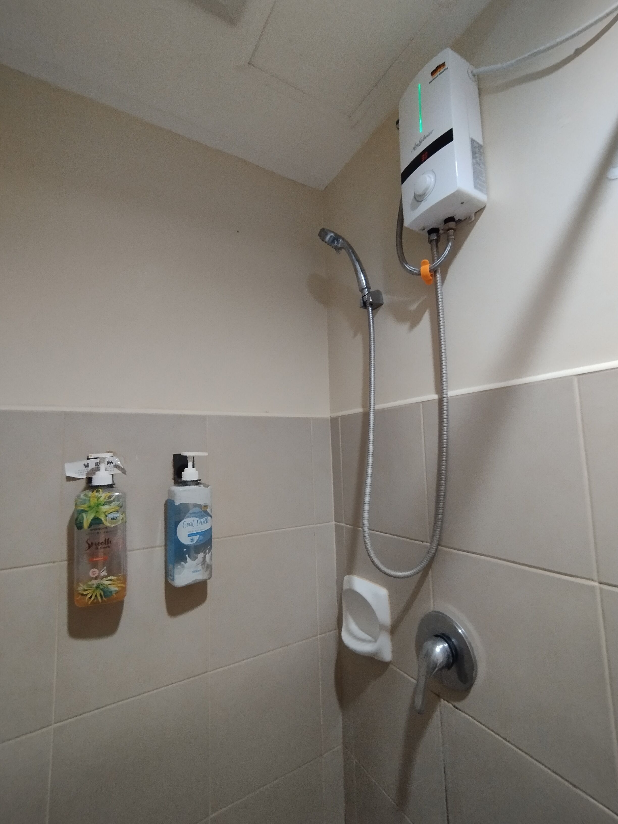 A shower area with a handheld showerhead, a wall-mounted faucet, and two bottles of liquid soap.