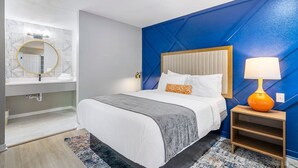 A modern hotel room with a large bed, a bedside table with a lamp, a bathroom with a mirror and sink, and a blue accent wall. - Modern Urban Oasis in Prime Buckhead, Atlanta (Atlanta)