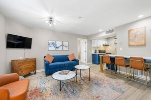 Una sala de estar moderna con sofá, mesa de centro, televisor y una cocina con taburetes de bar.