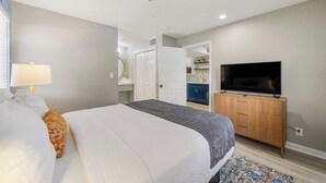 A hotel room with a bed, a TV, a dresser, and a bathroom visible through an open door.