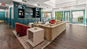 A spacious living area with a sofa, red chair, and a coffee table. There is a kitchen area with teal cabinets and a TV.