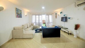 Ein Wohnzimmer mit einer Couch, einem blauen Sessel, einem Fernseher und einem Gemälde an der Wand.