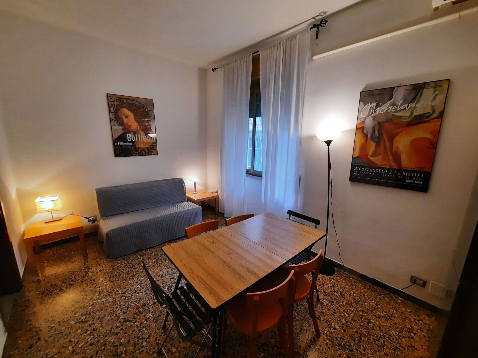 Et lille, møbleret rum med et træbord, to stole, en sofa, en lampe og et billede på væggen.