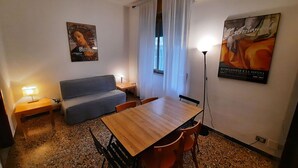 Ein kleiner, möblierter Raum mit Holztisch, zwei Stühlen, einer Couch, einer Lampe und einem Poster an der Wand.