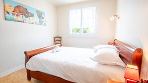 Una cama bien hecha con sábanas blancas, cabecera de madera y mesita de noche con lámpara.