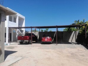 A parking area with two vehicles, a red pickup truck and a red car, under a covered structure.