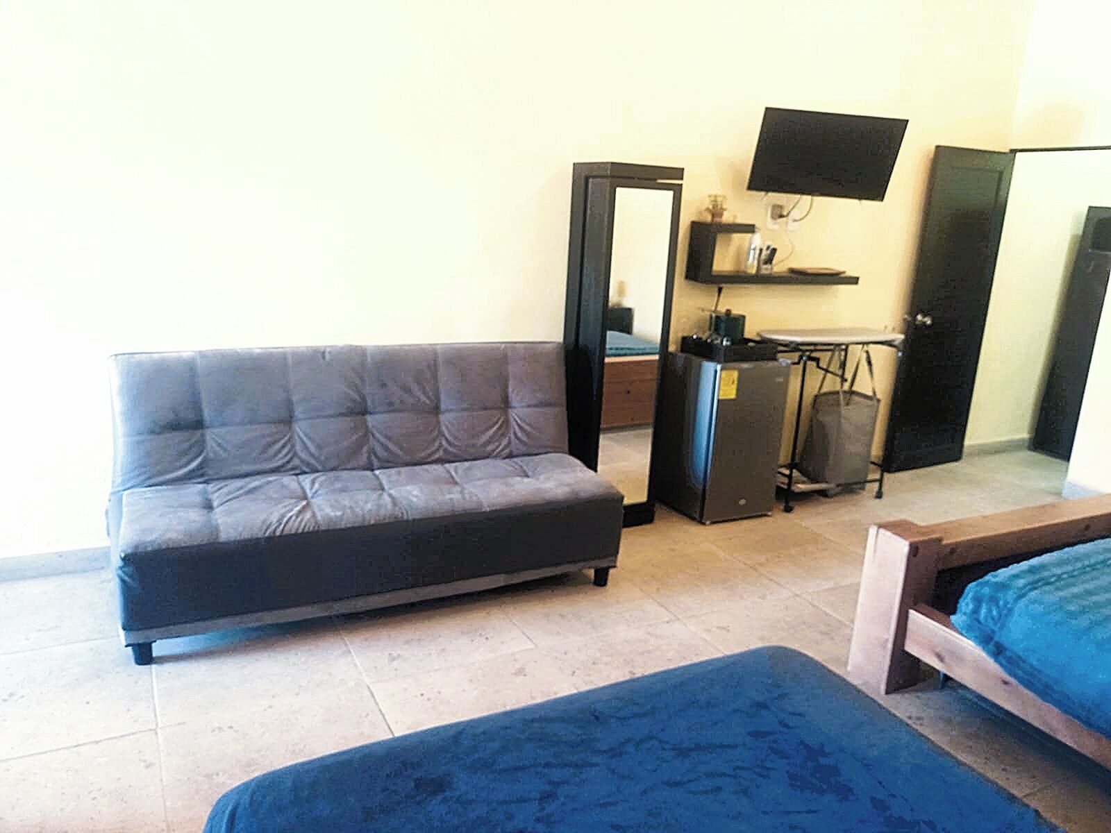 Una habitación con sofá, cama, escritorio con computadora, televisor y una puerta.